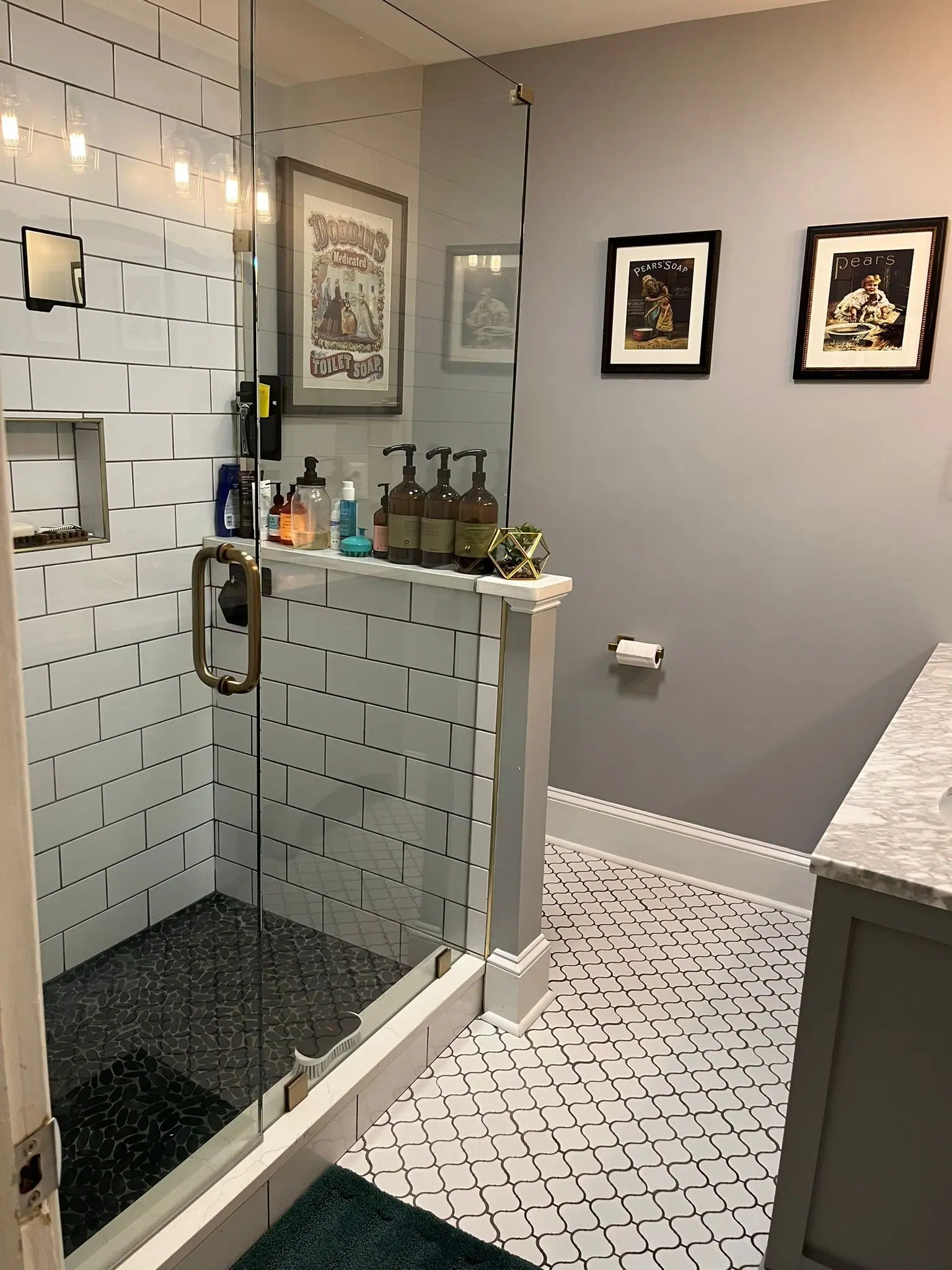 A bathroom with white subway tile shower, geometric patterned floor tiles, gray walls, and two framed wall pictures.