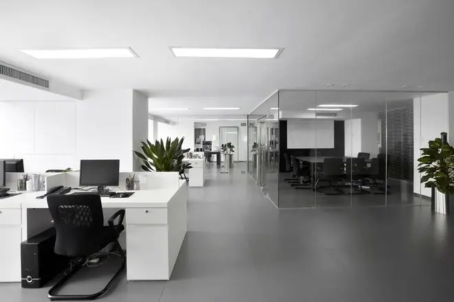 A modern office with white desks, black chairs, a glass-walled conference room, and plants on a gray…